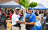 Two business owners shaking hands in front of a local outdoor festival