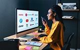 A woman viewing a group of corporate logos on a large PC screen on her desk